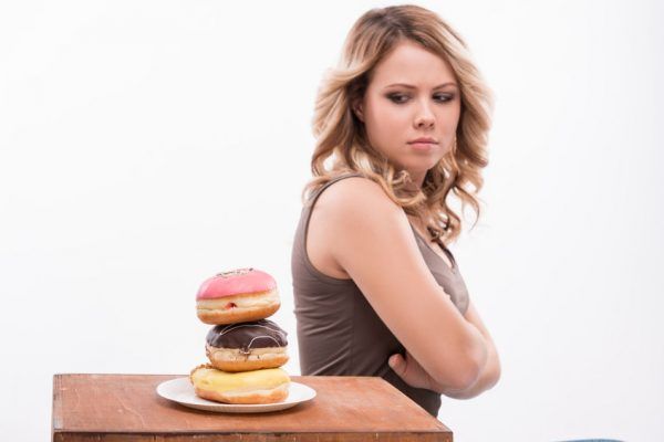 34868933 - portrait of young attractive woman looking at doughnuts doubtfully isolated on white background, diet concept